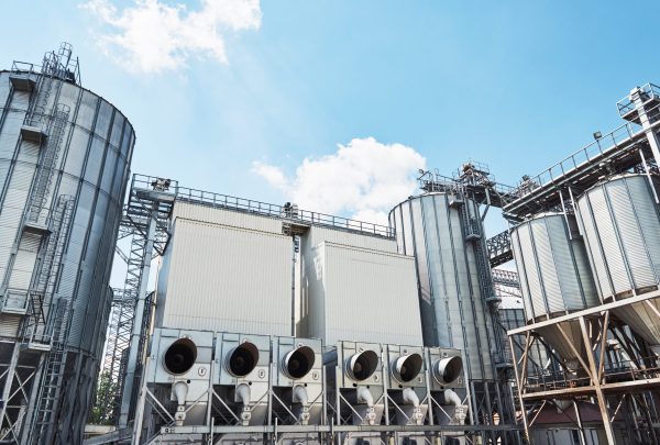 Agricultural Silos. Building Exterior. Storage and drying of grains, wheat, corn, soy, sunflower against the blue sky with white clouds Agricultural Silos. Building Exterior. Storage and drying of grains, wheat, corn, soy, sunflower against the blue sky with white clouds.