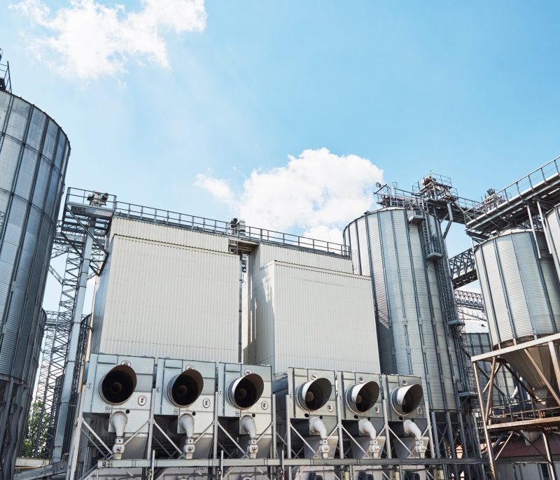 Agricultural Silos. Building Exterior. Storage and drying of grains, wheat, corn, soy, sunflower against the blue sky with white clouds.