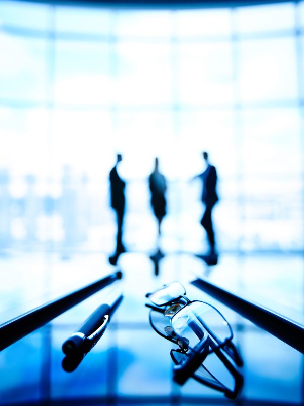 Image of eyeglasses and pen at workplace with businesspeople standing on the background