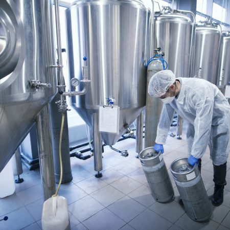 Worker in protective suit carrying chemicals in metal reservoirs.